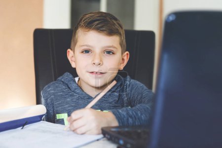 Photo for Happy healthy kid boy with glasses making school homework at home with notebook. Interested child writing essay with helping of internet. concetrated schoolchildren concept. - Royalty Free Image