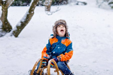Photo for Little school boy having fun with sleigh ride during snowfall. Hapy child sledding on snow. Preschool kid riding a sledge. Child playing outdoors in snowy winter park catching snowflake - Royalty Free Image