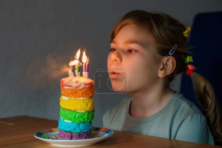 Photo for Happy little preschool girl celebrating birthday. Closeup of child with homemade rainbow cake, indoor. Happy healthy toddler blowing six candles on cake. Selective focus on cake. - Royalty Free Image