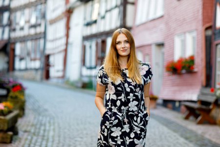 Schöne junge Frau mit langen Haaren im Sommerkleid, die in deutschen Städten spazieren geht. Glückliches Mädchen genießt Spaziergänge in netter Kleinstadt mit alten Häusern in Deutschland
