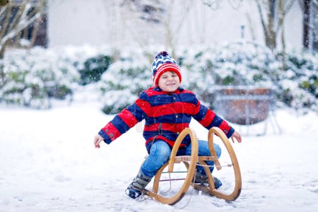 Photo for Little school boy having fun with sleigh ride during snowfall. Hapy child sledding on snow. Preschool kid riding a sledge. Child playing outdoors in snowy winter park. Active fun for family - Royalty Free Image