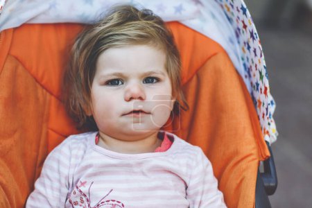 Foto de Retrato de una niña pequeña y sonriente sentada en un cochecito o cochecito de bebé y dando un paseo. Feliz bebé lindo que se divierte al aire libre. Hija sana - Imagen libre de derechos