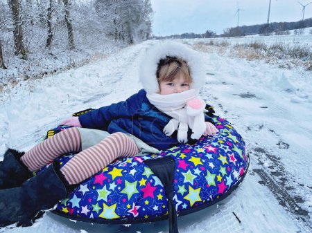 Foto de Active prechool girl sliding down the hill on snow tube. Cute little happy child having fun outdoors in winter on sledge . Healthy excited kid tubing snowy downhill, family winter time - Imagen libre de derechos