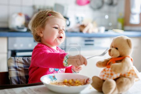 Photo for Adorable baby girl eating from fork vegetables and pasta. food, child, feeding and development concept. Cute toddler, daughter with spoon sitting in highchair and learning to eat by itself - Royalty Free Image