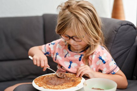 Photo for Adorable little girl having breakfast, eating pancakes with chocolate cream. Preschool child smiling. Sweet food for children - Royalty Free Image
