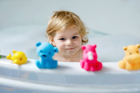 Téléchargez les photos : Adorable petite fille mignonne tout-petit prenant bain dans la baignoire. Bébé enfant heureux et en bonne santé jouant avec des jouets en gomme de caoutchouc et s'amusant. Lavage, nettoyage, hygiène pour les enfants - en image libre de droit
