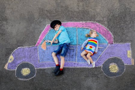 Foto de Dos niños pequeños, niño y niña se divierten con el dibujo de la imagen del coche con tiza de colores sobre asfalto. Los hermanos pintan en el suelo y juegan juntos. Ocio creativo para niños
. - Imagen libre de derechos