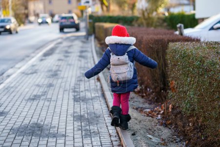 Photo for Cute little preschool girl with glasses on her the way to playschool. Healthy happy child walking to nursery school. Kindergarten kid with backpack going to day care on the city street, outdoors. - Royalty Free Image