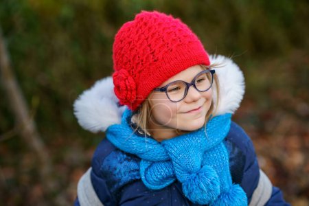 Téléchargez les photos : Cute little preschool girl with glasses on her the way to playschool. Healthy happy child walking to nursery school. Kindergarten kid with backpack going to day care on the city street, outdoors. - en image libre de droit