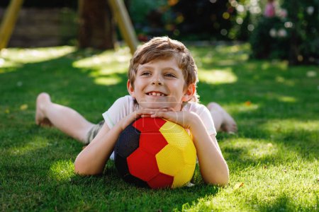Téléchargez les photos : Joyeux garçon actif jouant au football avec le ballon dans les couleurs du drapeau allemand. Enfant en bonne santé s'amuser avec le jeu de football et l'action en plein air
. - en image libre de droit