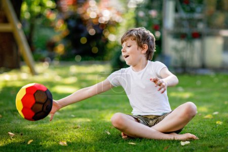 Foto de Feliz chico activo jugando al fútbol con pelota en colores de bandera alemana. Niño sano que se divierte con el juego de fútbol y la acción al aire libre
. - Imagen libre de derechos