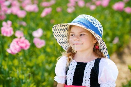 Téléchargez les photos : Little preschool girl in poppy field. Cute happy child in red riding hood dress play outdoor on blossom flowering meadow with pink poppies. Leisure activity in nature with children - en image libre de droit