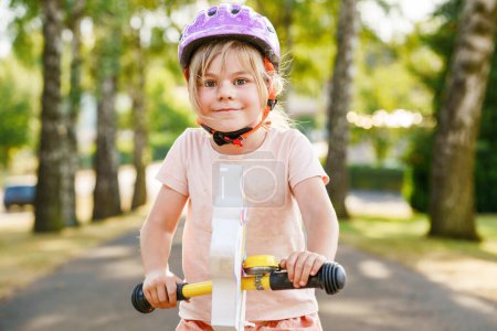 Téléchargez les photos : Petite fille d'âge préscolaire avec casque de course avec vélo d'équilibre le jour d'été. Bonne conduite de l'enfant, vélo avec vélo, activité de plein air. Bonheur, enfance. Activité estivale pour les enfants - en image libre de droit