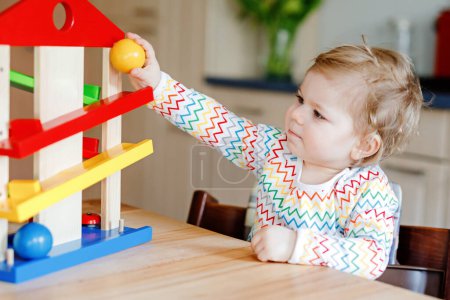 Photo for Little baby girl playing with educational toys at home or nursery. Happy healthy toddler child having fun with colorful wooden toy ball track. Kid learning to hold and roll balls. Motoric education - Royalty Free Image