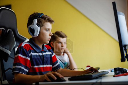 Téléchargez les photos : Deux enfants garçons jouant à des jeux informatiques sur PC de bureau. Activité de toxicomane moderne pour les enfants. Frères et amis jouant à la maison - en image libre de droit