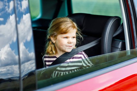 Photo for Adorable toddler girl sitting in car seat and looking out of the window on nature and traffic. Little kid traveling by car. Child safety on the road. Family trip and vacations. - Royalty Free Image