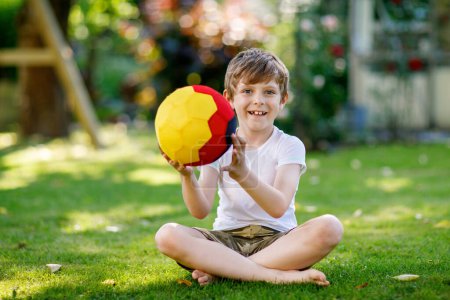 Photo for Happy active kid boy playing soccer with ball in German flag colors. Healthy child having fun with football game and action outdoors. - Royalty Free Image