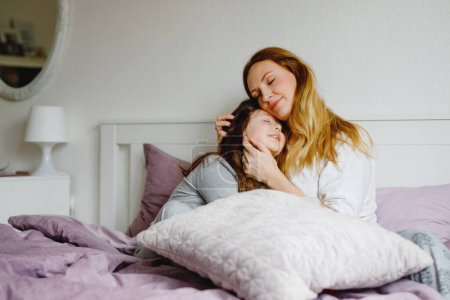 Photo for Lovely young mother and cute school kid girl cuddling together in bed in morning. Happy family of young single woman and beautiful daughter, indoors, getting ready and morning routine - Royalty Free Image