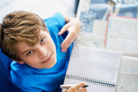 Téléchargez les photos : Un jeune garçon qui fait ses devoirs à la maison. Apprentissage scolaire - en image libre de droit