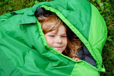Photo for Preschool little girl in sleeping bag camping. Outdoors activity with children in summer. Fun and adventure camp, family and friends vacations or weekend trip. Portrait of child with flashlight - Royalty Free Image