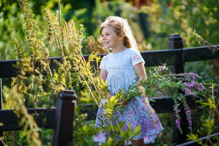 Foto de Retrato de una linda niña preescolar con flores silvestres al aire libre. Feliz niño divertido en la soleada noche de verano. - Imagen libre de derechos