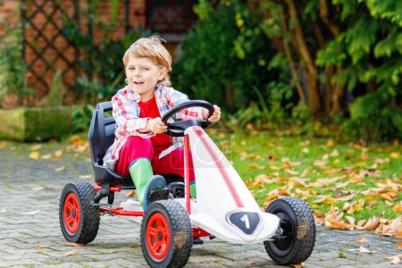 Photo for Funny little preschhool boy having fun and driving pedal race car in homes garden. Active games for children in summer. On warm sunny day. - Royalty Free Image