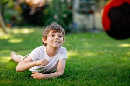 Téléchargez les photos : Joyeux garçon actif jouant au football avec le ballon dans les couleurs du drapeau allemand. Enfant en bonne santé s'amuser avec le jeu de football et l'action en plein air
. - en image libre de droit