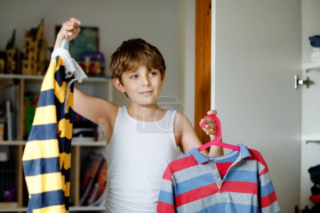 Photo for School kid boy standing by wardrobe with clothes. Child making decision for school shirt to wear. Children get dressed in the morning for school - Royalty Free Image