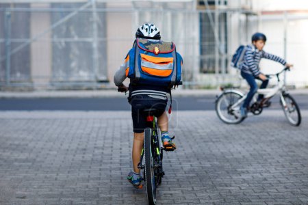 Foto de Dos niños de la escuela en casco de seguridad con bicicleta en la ciudad con mochilas. Niños felices en ropa colorida en bicicleta en bicicletas de camino a la escuela. Manera segura para los niños al aire libre a la escuela. - Imagen libre de derechos