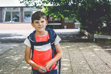 Photo for Kid boy with medical mask on the way to school. Child with backpack satchel. Back to school after summer holidays. Protection during corona pandemic. Healthy kid outdoors on school yard with building. - Royalty Free Image