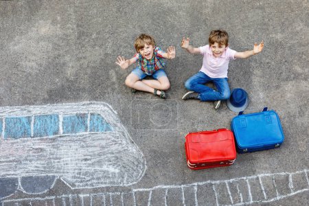 Téléchargez les photos : Deux petits garçons s'amusent avec le dessin d'image de train avec des craies colorées sur l'asphalte. Les enfants s'amusent avec la peinture à la craie et au crayon. partir en vacances et voyager. Amis avec valises
. - en image libre de droit