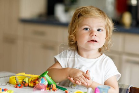 Téléchargez les photos : Adorable petite fille mignonne tout-petit avec de l'argile colorée. Bébé sain jouant et créant des jouets à partir de pâte à jouer. Petit enfant moulage modelage argile et apprentissage. - en image libre de droit