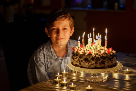 Photo for Adorable happy blond little kid boy celebrating his birthday. Preteen child blowing candles on homemade baked cake, indoor. Birthday party for school children, family celebration, teenager birthday. - Royalty Free Image