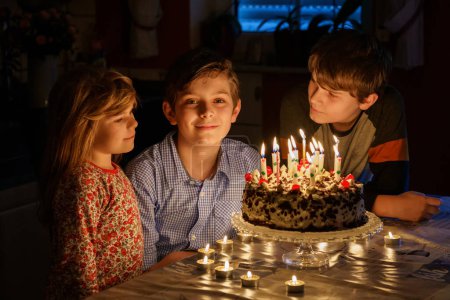 Photo for Happy preteen boy celebrating birthday. Preschool sister child and two kids boys brothers blowing together candles on cake. Happy healthy family portrait with three children siblings. - Royalty Free Image