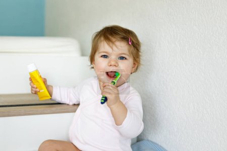 Téléchargez les photos : Petite fille tenant une brosse à dents et se brossant les premières dents. Enfant apprenant à nettoyer la dent de lait. Concept de prévention, d'hygiène et de santé. Enfant heureux dans la salle de bain. - en image libre de droit