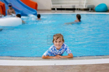 Foto de Niña preescolar jugando en la piscina al aire libre en el complejo hotelero. Niños aprendiendo a nadar en la piscina al aire libre, salpicando con agua, riendo y divirtiéndose. Vacaciones familiares - Imagen libre de derechos