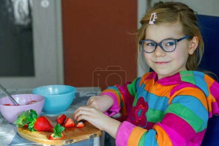 Foto de Littl preescolar aprender a usar un cuchillo de corte de fresa hacer ensalada de frutas para gachas para el desayuno en la cocina. Alimento saludable para niños - Imagen libre de derechos