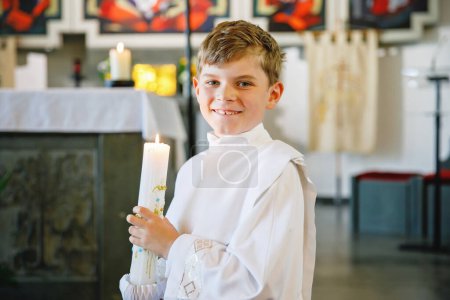 Photo for Little kid boy receiving his first holy communion. Happy child holding Christening candle. Tradition in catholic curch. Kid in a white traditional gown in a church near altar - Royalty Free Image