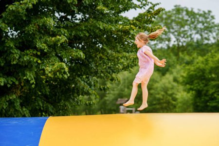 Téléchargez les photos : Petite fille d'âge préscolaire sautant sur trampoline. Heureux enfant tout-petit drôle s'amuser avec l'activité de plein air en été. Sports et exercices pour les enfants. Trampoline aux couleurs du drapeau ukrainien. - en image libre de droit