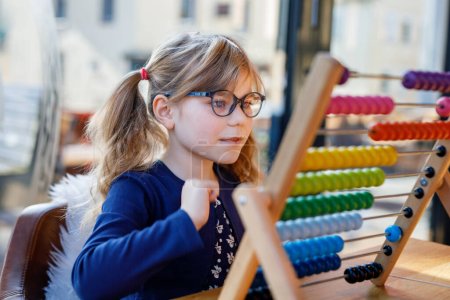 Photo for Little preschool girl playing with educational wooden rainbow toy counter abacus. Healthy happy child with glasses learning to count and colors, indoors on sunny day - Royalty Free Image