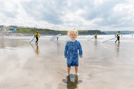 Foto de Little cute toddler girl at the Ballybunion surfer beach, having fun on with playing on west coast of Ireland. Happy child enjoying Irish summer and sunny day with family - Imagen libre de derechos