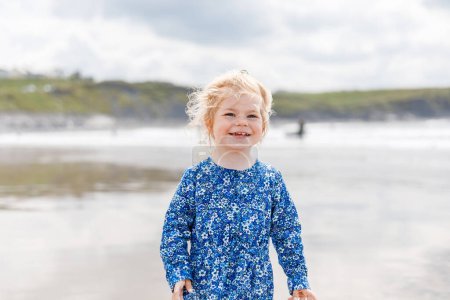 Téléchargez les photos : Little cute toddler girl at the Ballybunion surfer beach, having fun on with playing on west coast of Ireland. Happy child enjoying Irish summer and sunny day with family - en image libre de droit