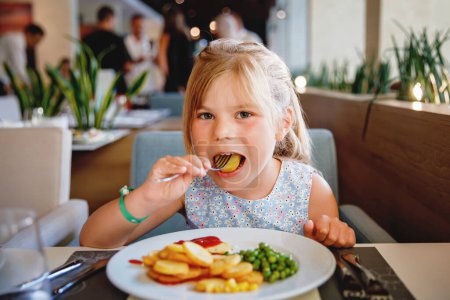Photo for Adorable little girl having breakfast at resort restaurant. Happy preschool child eating healthy food, vegetables and eggs in the morning - Royalty Free Image