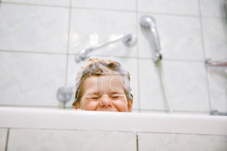 Foto de Lindo niño con espuma de champú y burbujas en el baño de toma de pelo. Retrato del feliz concepto de salud e higiene de la niña preescolar sonriente. Lava el cabello por sí misma - Imagen libre de derechos