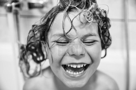 Téléchargez les photos : Enfant mignon avec mousse de shampooing et bulles sur les cheveux prenant un bain. Portrait de fille préscolaire souriante heureuse concept de soins de santé et d'hygiène. Se lave les cheveux toute seule - en image libre de droit