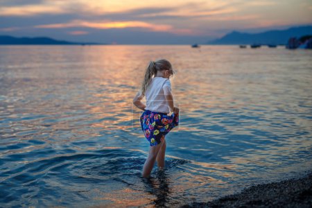 Téléchargez les photos : Petite fille marchant sur la belle plage de l'océan. Joyeux enfants d'âge préscolaire jouent au coucher du soleil sur la plage de la mer. Vacances en famille avec des enfants en été - en image libre de droit