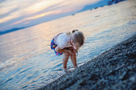 Téléchargez les photos : Petite fille marchant sur la belle plage de l'océan. Joyeux enfants d'âge préscolaire jouent au coucher du soleil sur la plage de la mer. Vacances en famille avec des enfants en été - en image libre de droit