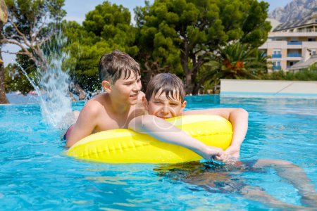 Foto de Dos niños se divierten en anillos de goma inflables en la piscina al aire libre. Vacaciones de verano. Fin de semana de verano para niños. Niños divirtiéndose, hermanos en vacaciones familiares - Imagen libre de derechos