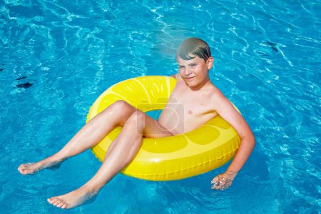 Photo for Cool school boy having fun on inflatable rubber circle in outdoor pool. Summer holiday. Summertime kids weekend. Child in swiming pool. Funny kid boy on ring at aquapark on family vacation - Royalty Free Image