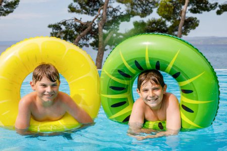 Foto de Dos niños se divierten en anillos de goma inflables en la piscina al aire libre. Vacaciones de verano. Fin de semana de verano para niños. Niños divirtiéndose, hermanos en vacaciones familiares - Imagen libre de derechos